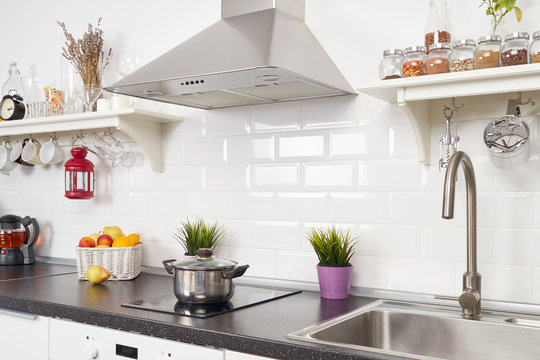 Interior of a light kitchen in the apartment. Bright home interior decoration items, fruit, flowers in a pot, steel hood. Bright ready-made picture for your individual design                     