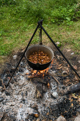 The cooking pot with goulash which is hanging on the tripod above campfire