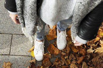 Young hipster woman is standing among autumn leaver wearing white sneakers. Top view. Autumn street fashion concept.