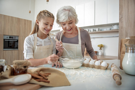 Happy granny and girl mixing meal with egg in bowl