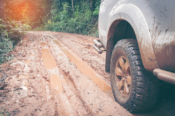 Fototapeta na wymiar Car wheel on a dirt road. Off-road tire covered with mud, dirt terrain. Outdoor, adventures and travel. Car tire close-up in a countryside landscape with a muddy road. Four wheel truck in mud.