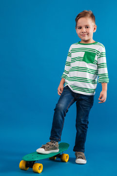 Full length image of smiling young boy posing with skateboard