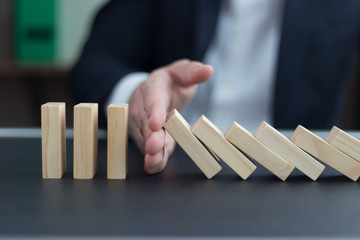 BUSINESSMAN HAND STOPPING DOMINO EFFECT CONCEPT