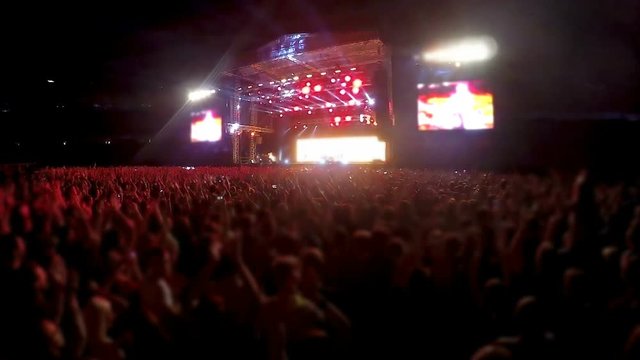 Thousands people standing in front of stage and clapping, rock band concert