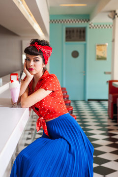 Portrait of beautiful roackabilly woman with milkshake at retro diner restaurant.