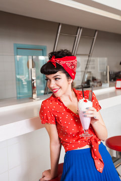 Handsome female in stylish retro outfit with milkshake at diner restaurant.