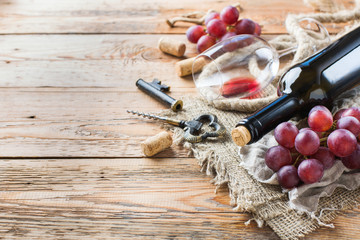 Bottle, corkscrew, glass of red wine, grapes on a table
