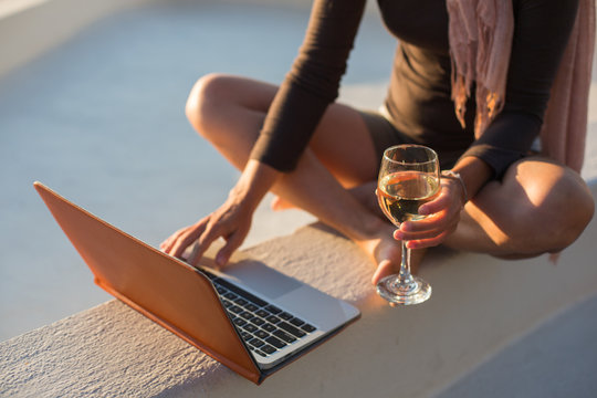Woman holding a glass of white wine with laptop
