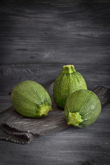 Green round zucchini on a dark wooden background. Rustic style, free space