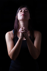 Faithful woman praying, hands folded in worship to god with head up and closed eyes in religious fervor, on a black background. Concept for religion, faith, prayer and spirituality.
