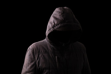 Naklejka na ściany i meble Scary and creepy man hiding in the shadows, with the face and identity hidden with the hood, and standing in the darkness. Low key, black background. Concept for fear, mystery, danger, crime, stalker