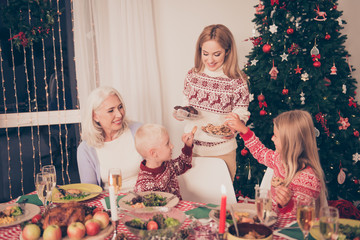 Cheerful relatives, setted festive desktop, full of yummy treats, apples, turkey, vegetables, cheerful siblings, granny, mom, decorated pine firtree, lights on windows, bon appetite!