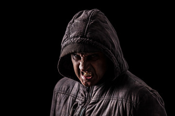 Very angry and aggressive man hiding in the shadows, with the face partly hidden with the hood, and standing in the darkness. Low key, black background. Concept for anger, rage, violence, danger © StockPhotosArt
