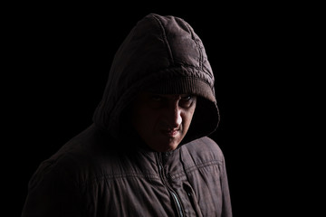 Man with repressed anger and violent instinct hiding in the shadows. Face partly hidden with hood, and standing in the darkness. Low key, black background. Concept for anger, rage, violence, danger