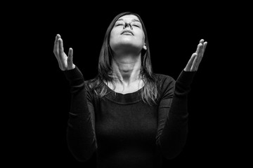 Mourning woman praying, with arms outstretched in worship to god, head up and eyes closed in suffer, on black background. Concept for religion, faith, prayer, grief, mourn, pain, depression. - obrazy, fototapety, plakaty