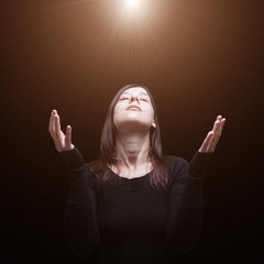 Mourning woman praying, with arms outstretched in worship to god, illuminated by a celestial or divine light. Concept for religion, faith, prayer, grief, mourn, pain, depression. © SPJE_ART