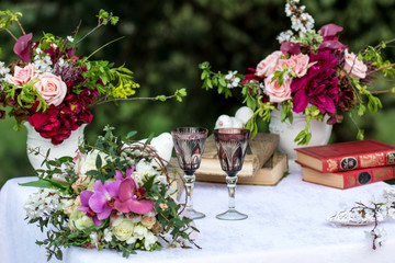 Wedding ceremony decoration arrangement flower bouquet wine glasses and books on the table covered with white cloth in the summer garden  