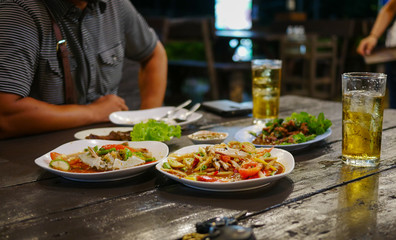 Dinning table in restaurant including Thai food,papaya salad etc. and two glasses of beer  with man sit in the opposite