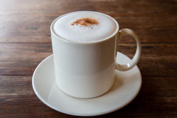 Cappuccino coffee in white cup on wooden table