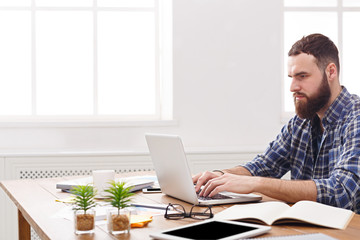 Fototapeta premium Pensive young businessman working with laptop in modern white office