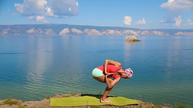 Beautiful slender woman practicing yoga at the edge of the cliff near lake baikal. Brunette girl doing yoga moves. Olkhon Island, Baikal, Russia, Siberia. Healthy Active Lifestyle concept