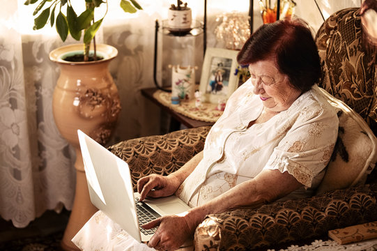 Senior woman using laptop sitting in chair at home