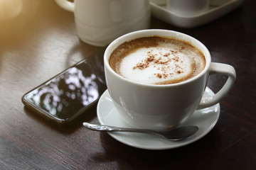 Coffee in a white cup on an old wood table and a smartphone.