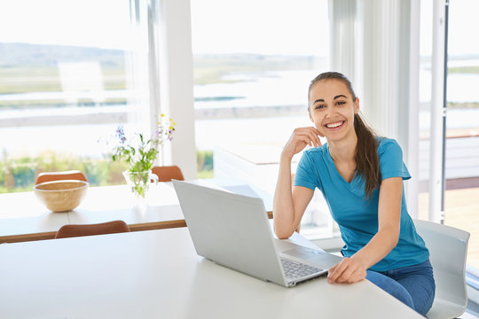 a young woman in casual clothes using the laptop computer in the living room or kitchen. freelance or remote work concept