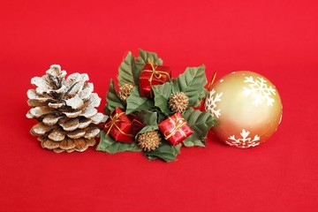 Une pomme de pin avec de la neige, des cadeaux rouges et une boule dorée sur un fond rouge pour décoration de fêtes