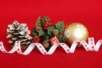 des cadeaux rouges sur une couronne de sapin, une pomme de pin avec de la neige dessus et une boule dorée pour la décoration de fêtes sur fond rouge
