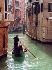 Fototapeta na wymiar Gondolier floats on the narrow channel in Venice, Italy