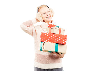 Portrait of senior woman in earmuffs holding heap of Christmas gifts