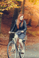 Fototapeta na wymiar Red haired girl riding on bike in autumnal park