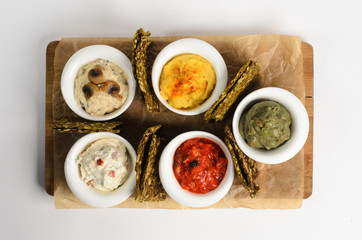 Appetizer of hummus, guacamole, veggie salsa, creamy cheese with sundried tomatoes and julienne with mushrooms with bread on a wooden desk isolated on white background