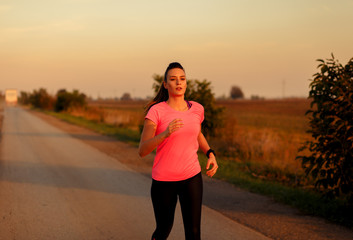 Athletic woman running on rural road during sunset.