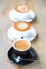 Three coffee cup on wooden table.first cup is black coffee,secound cup is cappuccino and the last one is latte.focus on the first coffee cup