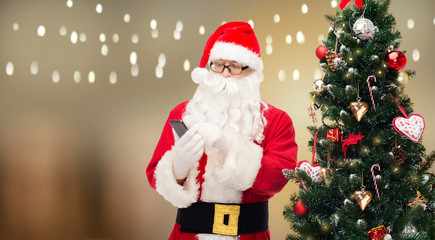 santa claus with smartphone at christmas tree