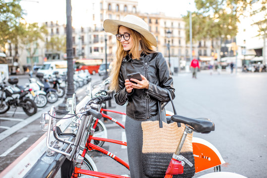 Young woman tourist renting a city bicycle with smartphone in Barcelona