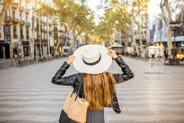 Young woman tourist in hat walking on the famous pedestrian boulevard in Barcelona city - obrazy, fototapety, plakaty