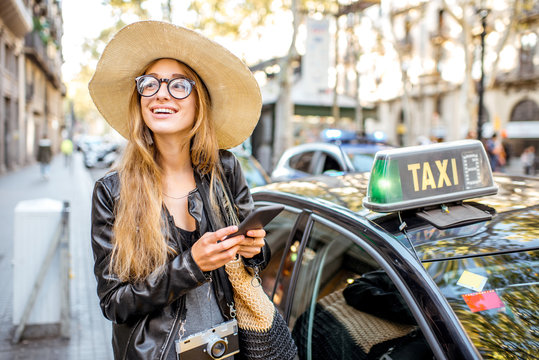 Young woman tourist using a smart phone standing near a taxi car on the street in Barcelona city
