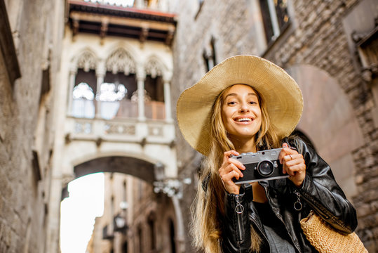 Young woman tourist in hat standing with photo camera in front of the famous bridge of sighs in Barcelona old town
