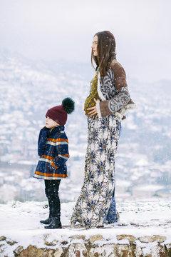 Beautiful pregnant woman with her little son outside while snowing