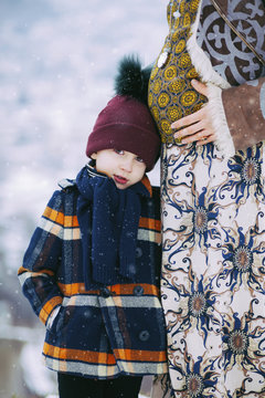 Beautiful pregnant woman with her little son outside while snowing