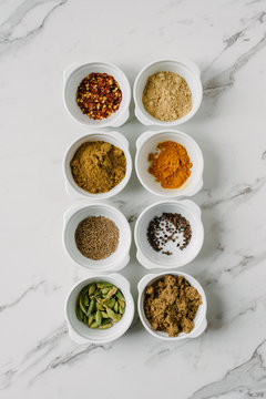 8 little bowls filled with various spices and seeds on a marble background