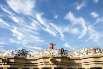Naklejka premium View on the beautiful terrace decorated with mosaic with happy woman tourist in Guell park in Barcelona. Wide angle view with copy space