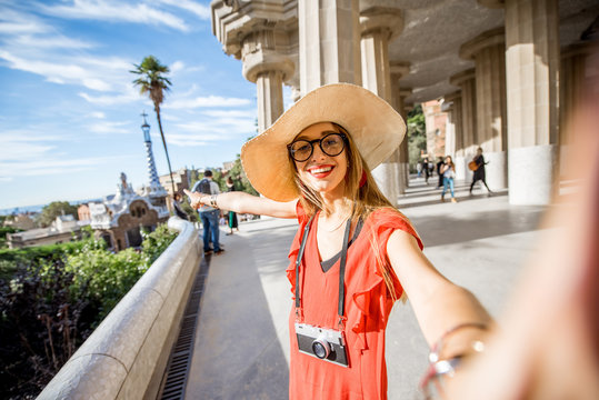 Happy woman tourist in red dress with hat standing near the columns visiting famous Guell park in Barcelona