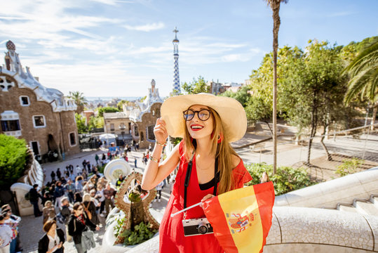 Woman tourist in red dress enjoying great view standing with spanish flag on the terrace in famous Guell park in Barcelona