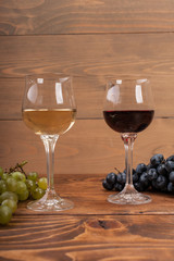 Red and white wine glasses and grape on wooden table