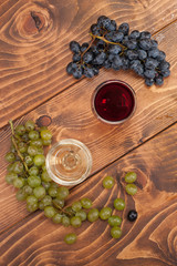 Red and white wine glasses and grape on wooden table