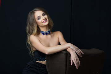 Naklejka premium portrait of a smiling beautiful young girl with makeup and hairdress on head on a black background